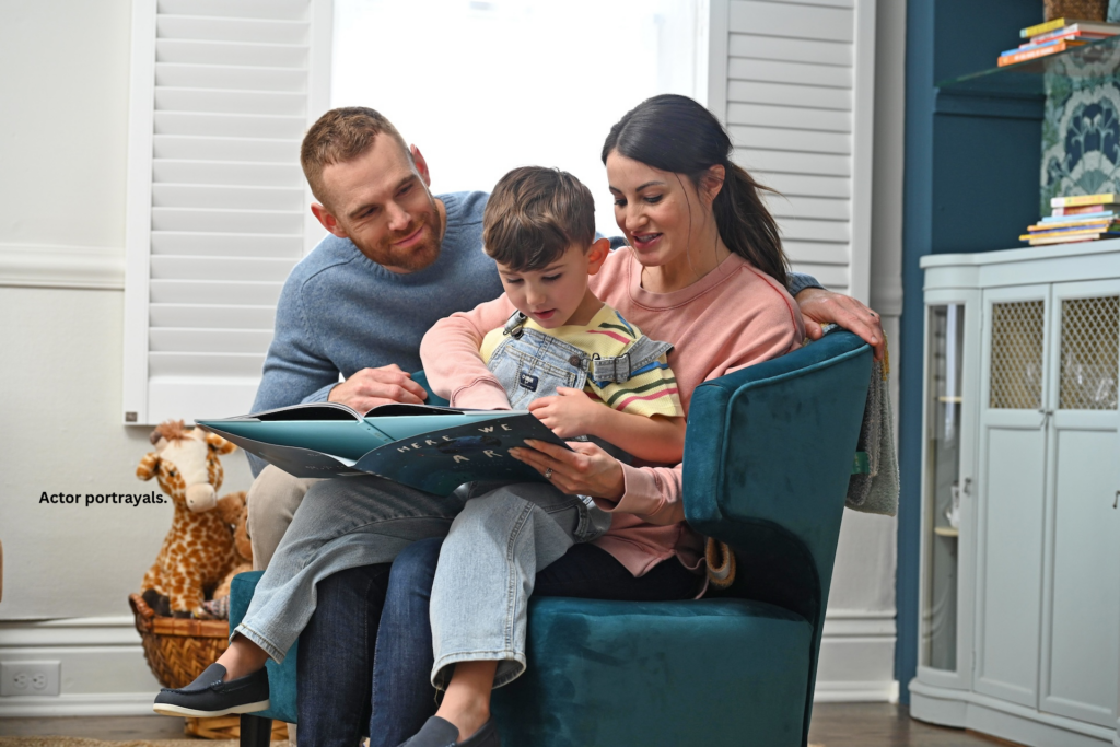 A family of 3 sitting in child'a room reading a book. The son is sitting on the mother's lap and the father is kneeling beside them.